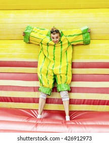 Joyful Young Caucasian Woman In Plastic Dress In A Bouncy Castle Imitates A Fly On Velcro Wall. Inflatable Attraction. Leisure Activity. Crazy Woman. Free Time Activities. Vertical Composition.