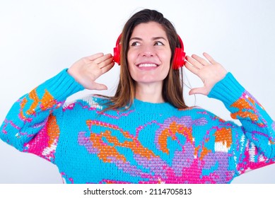 Joyful Young Caucasian Woman Wearing Vintage Colorful Sweater Over White Background Sings Song Keeps Hand Near Mouth As If Microphone Listens Favorite Playlist Via Headphones