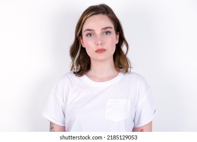 Joyful young caucasian woman wearing white T-shirt over white background looking to the camera, thinking about something. Both arms down, neutral facial expression. - Powered by Shutterstock