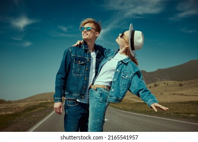 Joyful young couple wearing jeans clothes and black sunglasses stands on a highway smiling and hugging each other. Denim style. Freedom and independence concept.  - Powered by Shutterstock