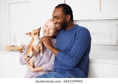 Joyful young diverse couple holding dog and spending time at home - Powered by Shutterstock