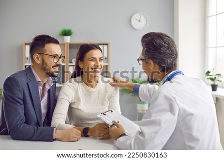 Joyful young family couple planning pregnancy and visiting doctor. Medical specialist sitting at desk with happy man and woman, talking about IVF treatment, and reassuring them