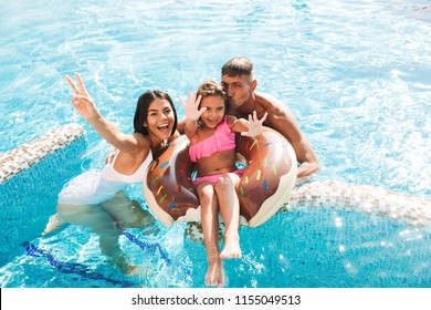 Joyful young family having fun together at the swimming pool outdoors in summer, swimming with inflatable ring donut