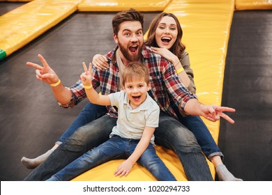 Joyful young family with their little son spending time on a trampoline together at the entertainment centre