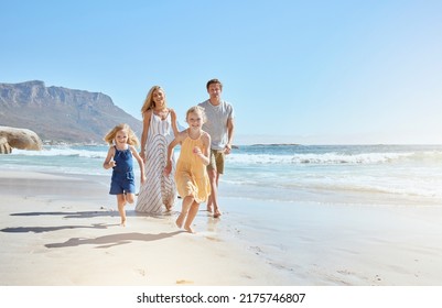 Joyful young family with two children running on the beach and enjoying summer vacation. Two energetic little girls running ahead while their mother and father follow in the background - Powered by Shutterstock
