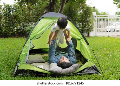 Joyful Young Father In Casual Wear Sets Up A Camping Tent In Family Home Outdoor Garden With Happy Little Son And Having Fun Together With Children Toy And Laptop