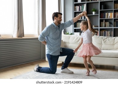 Joyful young father standing on one knee, raising arms twisting little funny preschool kid daughter, dressed as princess in living room. Happy different generations family dancing to music at home. - Powered by Shutterstock