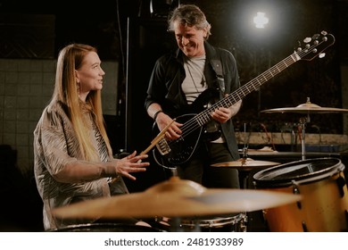 Joyful young female drummer and mature male bassist talking while having rehearsal in garage - Powered by Shutterstock