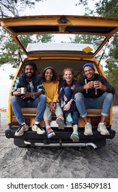 Joyful Young Friends Resting At Their Car While Enjoying Their Weekend In The Forest. Camping Concept