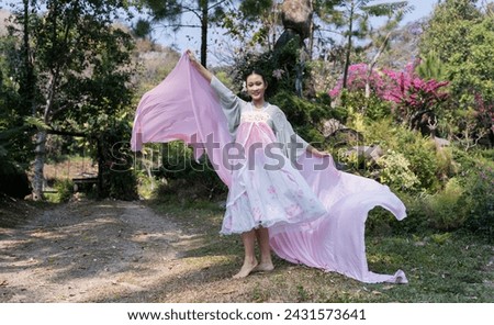 A joyful young girl dancing with a flowing scarf made of thin long fabric in wind. cape train fluttering fly in wind in garden