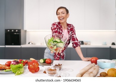 Joyful Young Housewife Holding Bawl Of Salad Showing It On Camera In Her New Kitchen Of A New House Prepared For A Family Dinner Or Girls Night Standing In The Kitchen. New House Concept. 