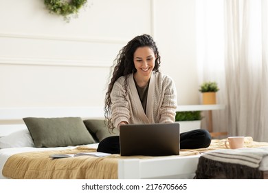 Joyful Young Lady Sitting Cross Legged On Bed, Using Laptop For Online Work Or Education At Home, Copy Space. Lovely Millennial Female Studying Remotely, Having Business Meeting On Web