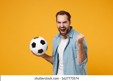 Joyful Young Man In Blue Shirt Posing Isolated On Yellow Orange Wall Background. People Sincere Emotions Lifestyle Concept. Mock Up Copy Space. Holding Soccer Ball, Doing Winner Gesture, Screaming