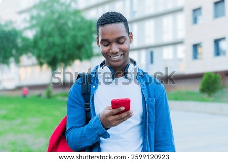 Joyful young man happily engaged with his smartphone while enjoying a moment of leisure and connection in a vibrant campus atmosphere filled with youthful energy and enthusiasm