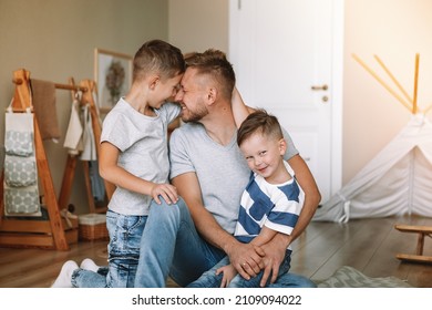 Joyful Young Man Lying On The Floor Picking Up Excited Happy Little Son At Home. Two Sons And A Father. Carefree Family Of Two Generations Having Fun. Daddy's Care And Strength.