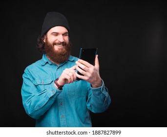 A Joyful Young Man Is Typing A Message On His Brand New Tablet Near A Dark Wall