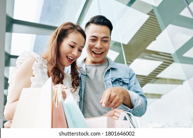 Joyful Young Man And Woman Looking Inside Bag With Purchases They Made In Mall