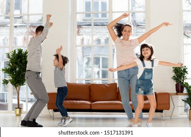 Joyful Young Mommy Jumping With Adorable Daughter, Happy Father Dancing With Cute Son To Favorite Energetic Music Tracks In Living Room At Home. Joyful Family Enjoying Dancing Party In Living Room.