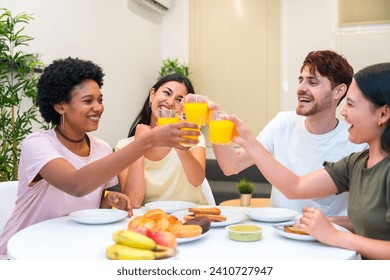 Joyful young multi-ethnic friends toasting with orange juice having breakfast at home - Powered by Shutterstock