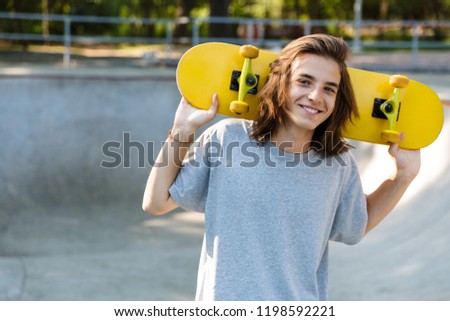 Joyful young teenge boy spending time at the skate park, holding a skateboard