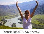 Joyful young woman with arms raised and eyes closed, enjoying mountain view on top of Mount Camel near Chemal, Altai Republic, Russia. Hiking happiness, travel emotions and nature adventure concept