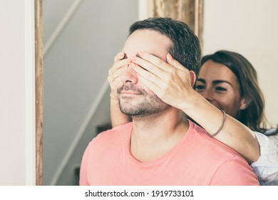 Joyful Young Woman Covering His Boyfriend Eyes With Hands And Leading Him Into Their New Apartment. Family Couple Walking Through Doorway. Medium Shot. New Home Or Surprise Concept