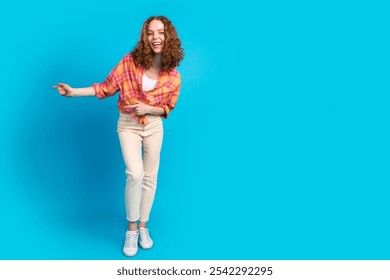 Joyful young woman with curly hair in vibrant plaid shirt dancing against bright blue background - Powered by Shutterstock