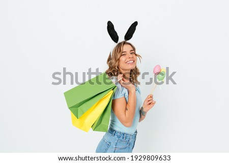 Joyful young woman holding decorative Easter eggs and shopping bags while standing against white background.