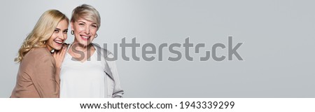 joyful young woman leaning on shoulder of stylish mother isolated on grey, banner