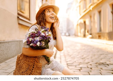 A joyful young woman on the cobblestone street, wearing a summer dress and a sun hat, holding a fresh bouquet of colorful flowers. Fashion style. - Powered by Shutterstock