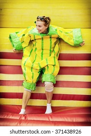 Joyful Young Woman In Plastic Dress In A Bouncy Castle Imitates A Fly On Velcro Wall. Inflatable Attraction. Leisure Activity.