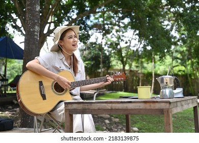 Joyful Young Woman Playing Guitar During Camping Alone Near River Bank On Beautiful Day