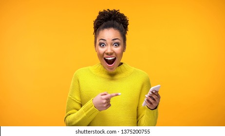 Joyful young woman pointing at smartphone in hand, online shopping application