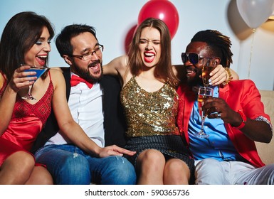 Joyful Young Woman In Shiny Top Slightly Embracing Her Asian And Afro-American Friends While Posing For Photography During Lovely House Party