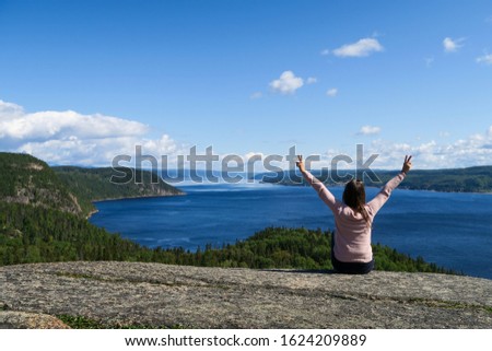 Joyful young woman sitting on a rock admiring the beautiful Saguenay fjord