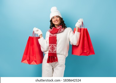 Joyful Young Woman In Winter Outfit Holding Red Shopping Bags And Looking Up On Blue