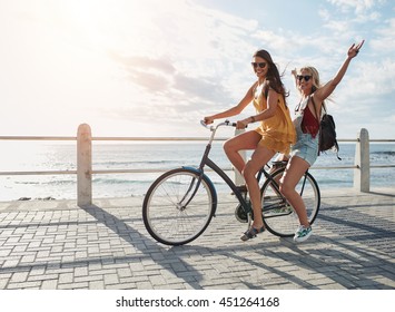 Joyful young women riding a bicycle together. Best friends having fun on a bike at the seaside promenade.