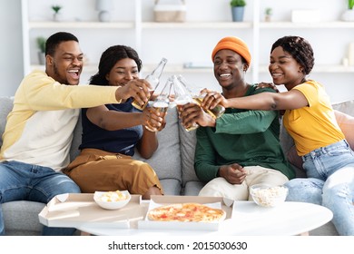 Joyfull African American Millennial Friends Eating Pizza In Living Room, Cheering With Beer, Having Conversation, Laughing And Smiling, Enjoying Time Together, Black Fellows Having Home Party