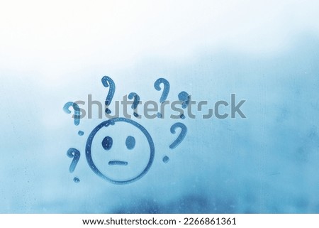 joyless smile face with question marks around head painted on blue window flooded with raindrops on blur glass background in city