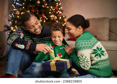 joyous african american family smiling and hugging lovingly next to Christmas tree with garlands - Powered by Shutterstock