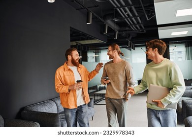 joyous bearded entrepreneur holding coffee to go and talking to business partners with smartphone and laptop walking in contemporary lounge of coworking space, successful collaboration - Powered by Shutterstock