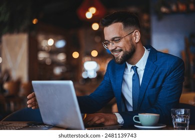 A joyous Caucasian male in a sharp suit works diligently on his laptop, surrounded by the warm ambiance of a local coffee house, cup nearby. - Powered by Shutterstock