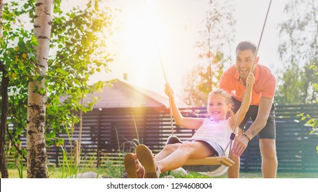 Joyous Father Pushes Swings with His Cute Little Daughter on Them. Happy Family Spends Time Together one Sunny Summer Day in the Idyllics Backyard. - Shutterstock ID 1294608004