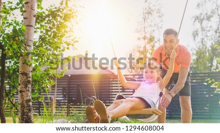 Joyous Father Pushes Swings with His Cute Little Daughter on Them. Happy Family Spends Time Together one Sunny Summer Day in the Idyllics Backyard.