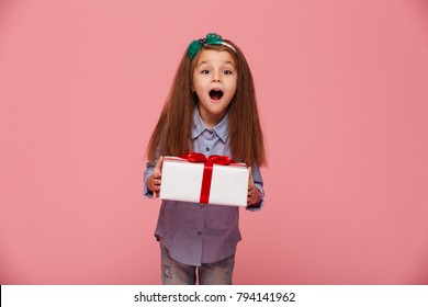 Joyous Female Kid Shouting Holding Gift-wrapped Box Being Excited And Surprised To Get Birthday Present, Over Pink Background