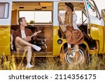 joyous hipster couple playing guitar ukulele sing a song in yellow van, in nature, field in countryside. traveler traveling together with vintage mini van in camping tent. camper vacation outdoors