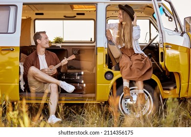 joyous hipster couple playing guitar ukulele sing a song in yellow van, in nature, field in countryside. traveler traveling together with vintage mini van in camping tent. camper vacation outdoors - Shutterstock ID 2114356175