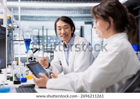 Joyous lab scientists using tablet to evaluate genetic markers associated with disease risk. Smiling senior researcher and colleague study DNA strand mapping with genomics analysis app on device