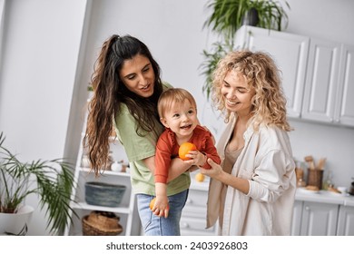 joyous lesbian couple having fun together with their cute baby girl holding tangerines, family - Powered by Shutterstock