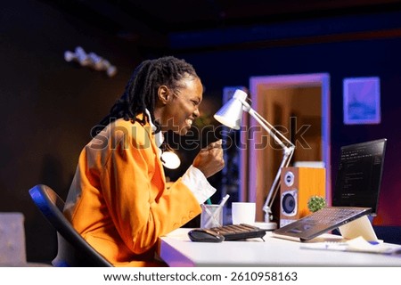 Joyous programmer at desk typing code on laptop, delighted after successfully developing software program. Thrilled african american woman at home excited after implementing new features